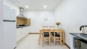 Una cocina compacta con armarios blancos, una campana extractora de acero inoxidable, una mesa de madera con sillas y una cafetera en la encimera.