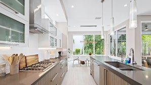 A modern kitchen with a central island, stainless steel appliances, and a view to the outdoors. - Beachside Bliss | Luxury Villa with Sauna & Pool (Fort Lauderdale)