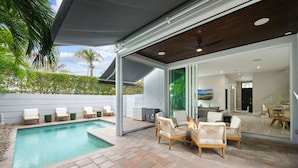 A modern outdoor pool area with lounge chairs, a covered seating area, and a view of the interior. - Beachside Bliss | Luxury Villa with Sauna & Pool (Fort Lauderdale)