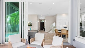 A modern living room with a fireplace, wicker furniture, and a view of the outdoors. - Beachside Bliss | Luxury Villa with Sauna & Pool (Fort Lauderdale)