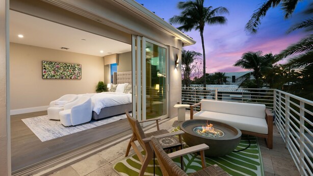 A modern bedroom with a bed, a sofa, and a fire pit on a balcony. - Beachside Bliss | Luxury Villa with Sauna & Pool (Fort Lauderdale)