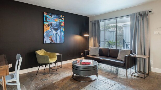 Ein modernes Wohnzimmer mit schwarzer Wand, großem Fenster mit Vorhängen, einer schwarzen Couch, einem gelben Sessel, einem runden Couchtisch und einem Gemälde.