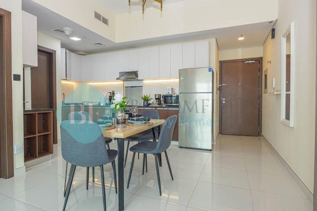 A modern kitchen with white cabinets, a stainless steel refrigerator, and a dining area with a wooden table and chairs.