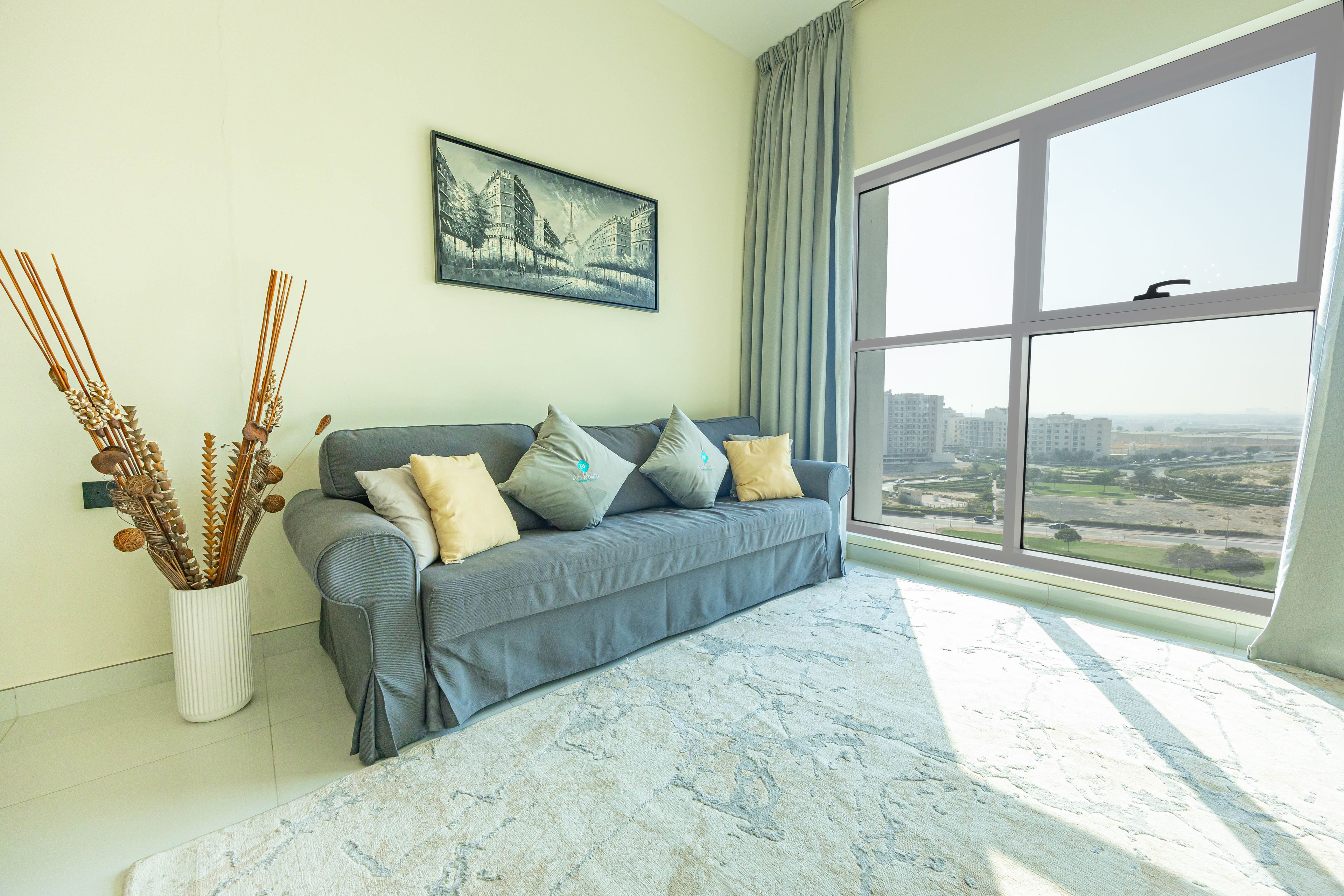 Een moderne woonkamer met een grijze bank, een groot raam en een schilderij aan de muur.