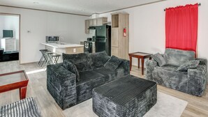 Un soggiorno moderno con un divano nero, un piccolo tavolo in legno e un angolo cottura con frigorifero e microonde.