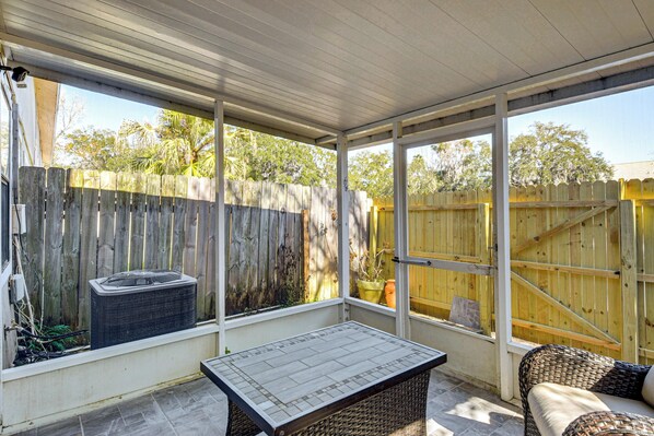 A covered patio with a table and wicker furniture, wooden fences, and a potted plant. - Sun, Sand & Poolside Relaxation! Ormond Beach Unit (Ormond Beach)