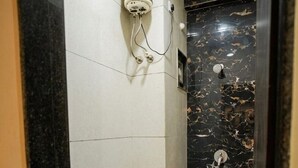 A bathroom with a toilet, a shower, and a marble wall. - Hotel Mokshita (Indore)