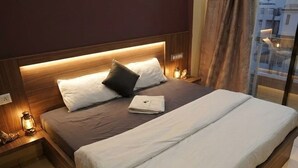 A modern hotel room with a large bed, wooden headboard, and a view of the city through a large window. - Hotel Mokshita (Indore)