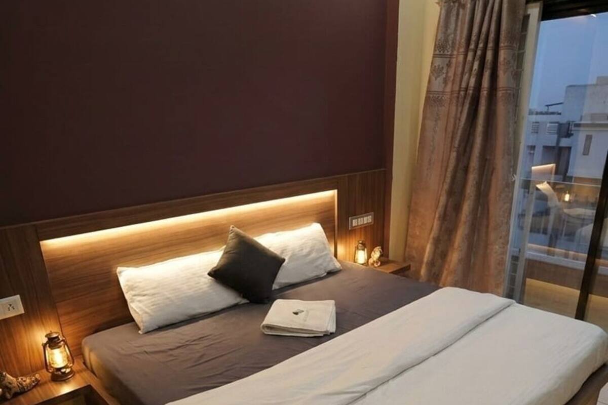 Habitación de hotel moderna con una cama grande, cabecera de madera y vista a la ciudad a través de un amplio ventanal.