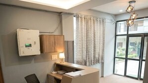 A reception desk with a modern design, a large window with curtains, and a ceiling light fixture. - Hotel Mokshita (Indore)
