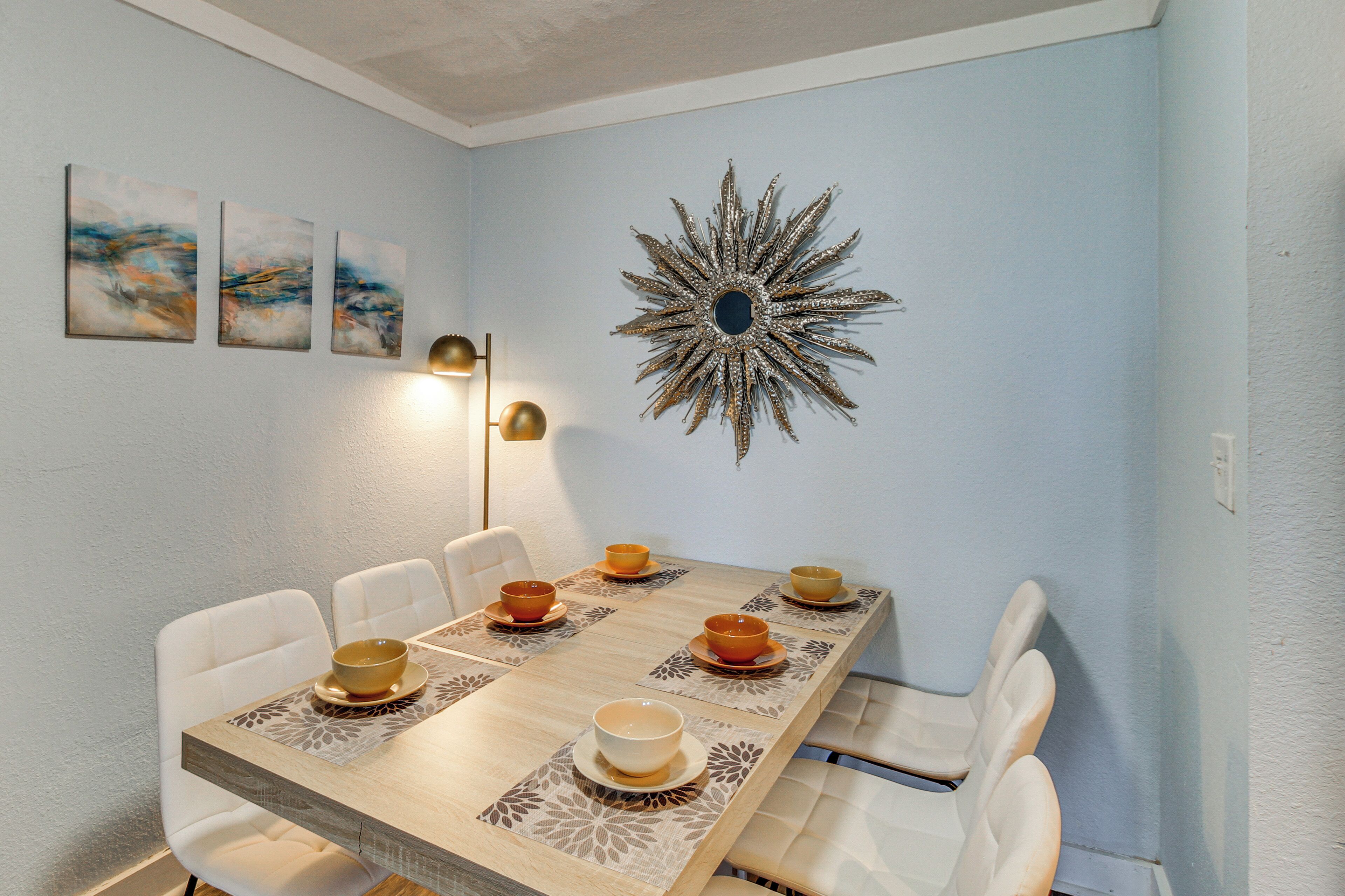 A dining area with a wooden table, white chairs, and a decorative wall piece.
