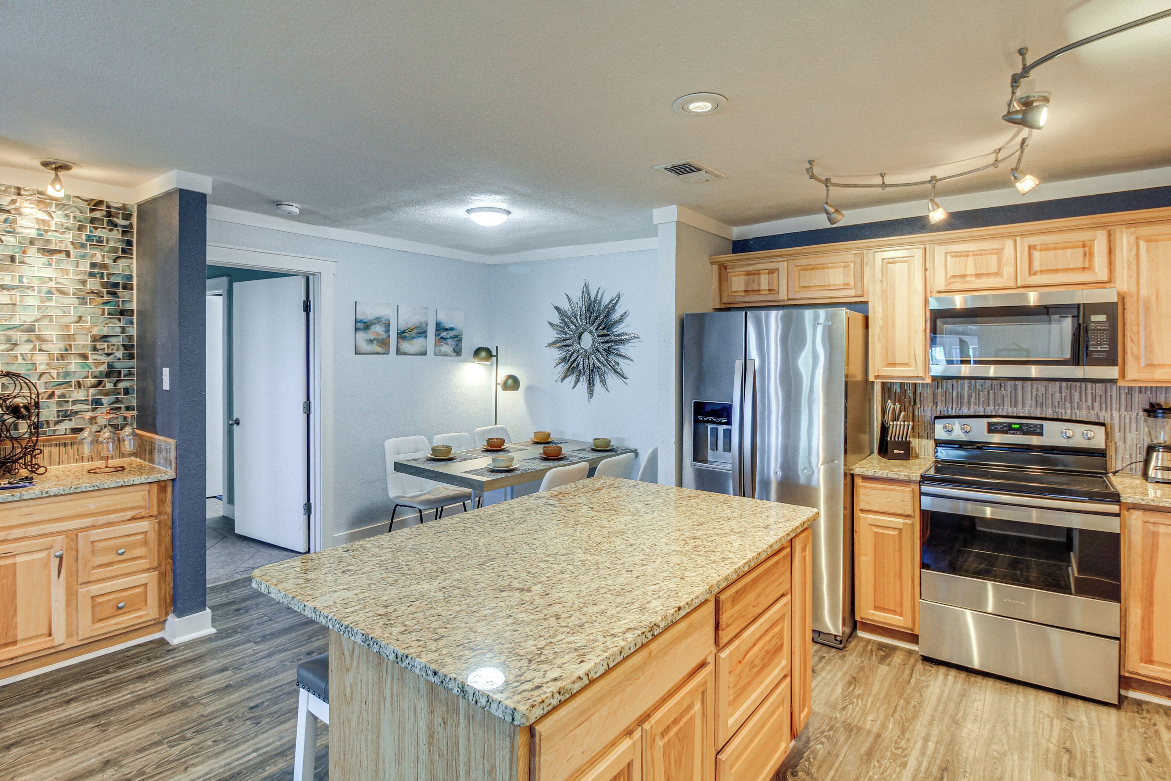 Una cocina moderna con encimeras de granito, electrodomésticos de acero inoxidable, armarios de madera y una zona de comedor con mesa y sillas.