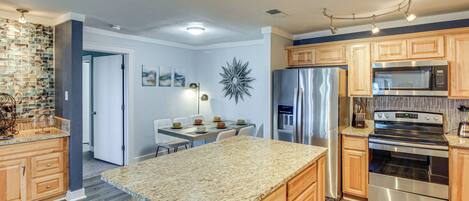 Una cocina moderna con encimeras de granito, electrodomésticos de acero inoxidable, armarios de madera y una zona de comedor con mesa y sillas.