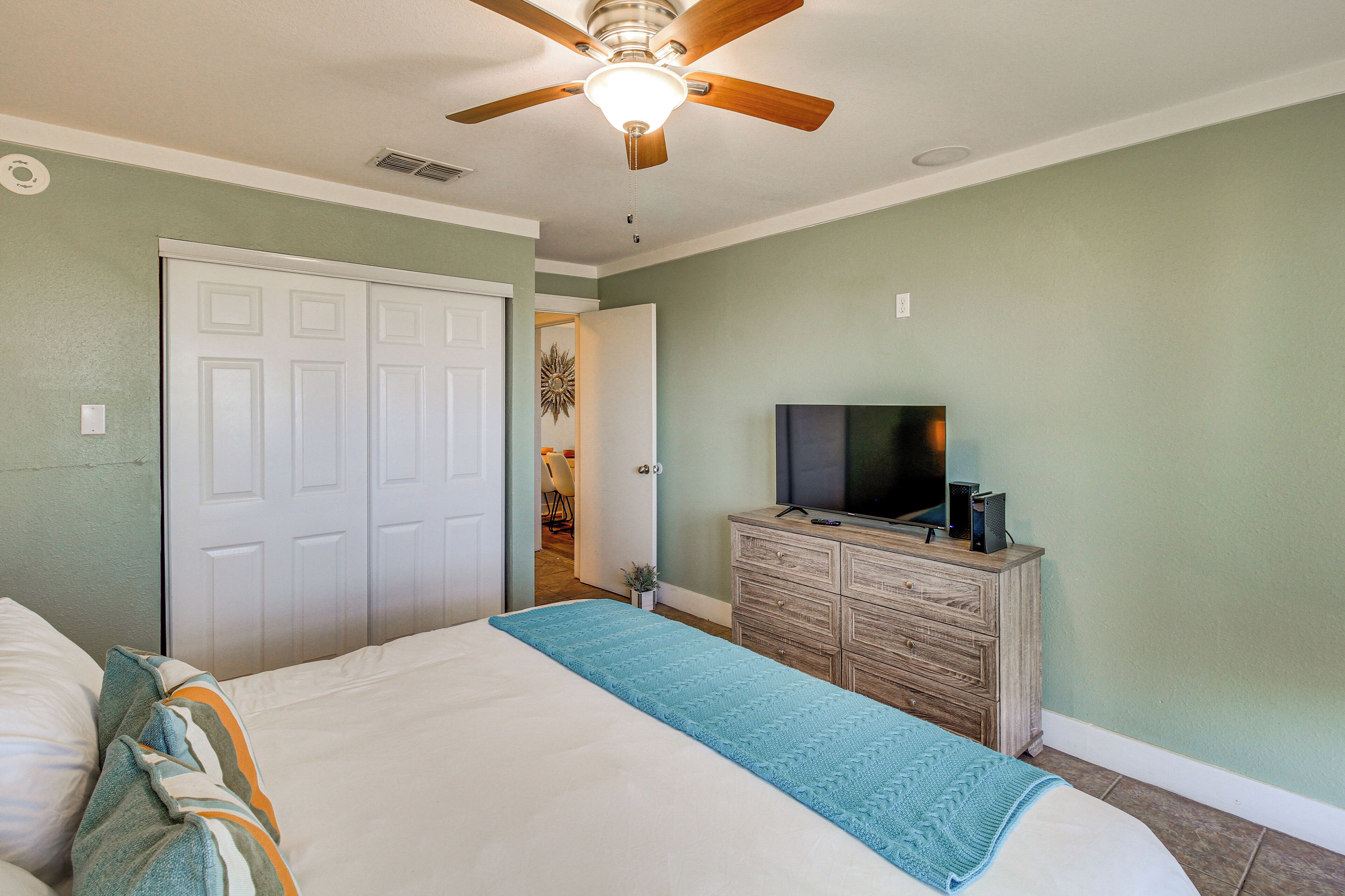 A bedroom with a bed, a ceiling fan, a dresser, a television, and a door.