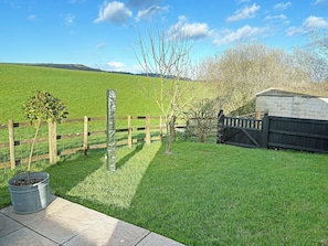 A fenced outdoor area with a grassy field, a wooden fence, a metal post, and a brick wall. - 1 bedroom accommodation in Bridport (Bridport)