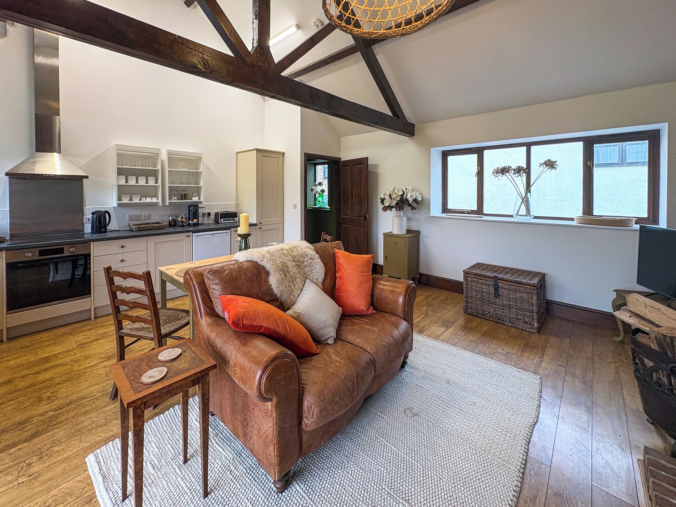 A spacious living area with a brown leather sofa, a wooden dining table, and a kitchen in the background.