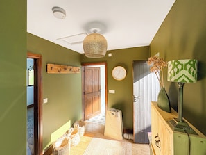 A hallway with a wooden door, a wall clock, a hanging light fixture, and a lamp on a cabinet. - 1 bedroom accommodation in Bridport (Bridport)