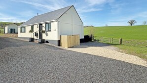 Un bâtiment blanc avec un toit en pente, une allée gravillonnée et une clôture en bois.