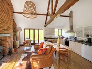 A spacious living area with a leather sofa, a dining table, and a kitchen with white cabinets. - 1 bedroom accommodation in Bridport (Bridport)