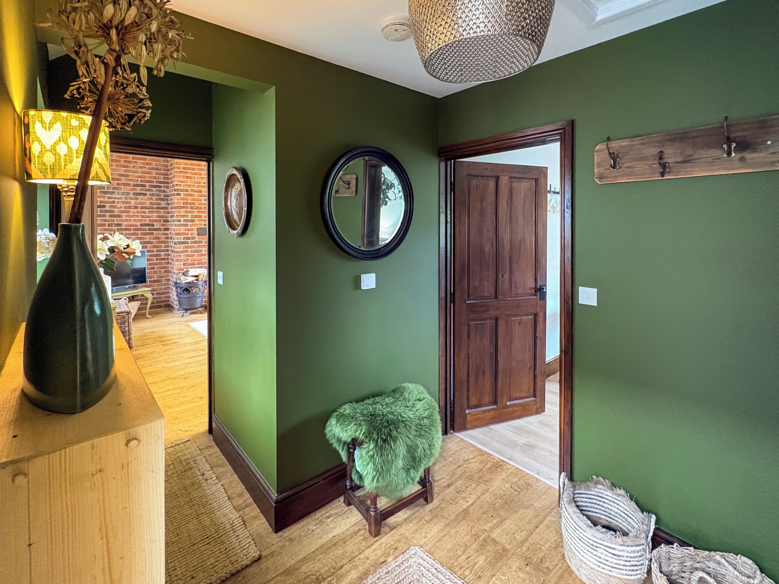 Un couloir aux murs verts, une porte en bois, un miroir et un petit tabouret.