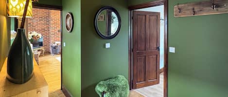 Un pasillo con paredes verdes, una puerta de madera, un espejo y un taburete pequeño.