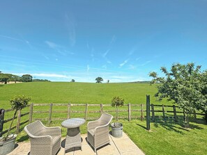 Een terras buiten met rieten meubels en uitzicht op een groen veld.