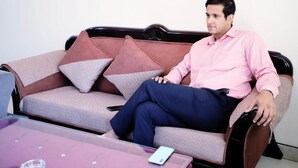 A man sitting on a sofa with a laptop and a remote control on a table in front of him. - Fortune Home Service Apartment J-171 (New Delhi)