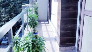 A balcony with potted plants, a metal railing, and a door with a dark frame. - Fortune Home Service Apartment J-171 (New Delhi)