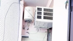 A small balcony with a potted plant, a black refrigerator, and an air conditioning unit. - Fortune Home Service Apartment J-171 (New Delhi)