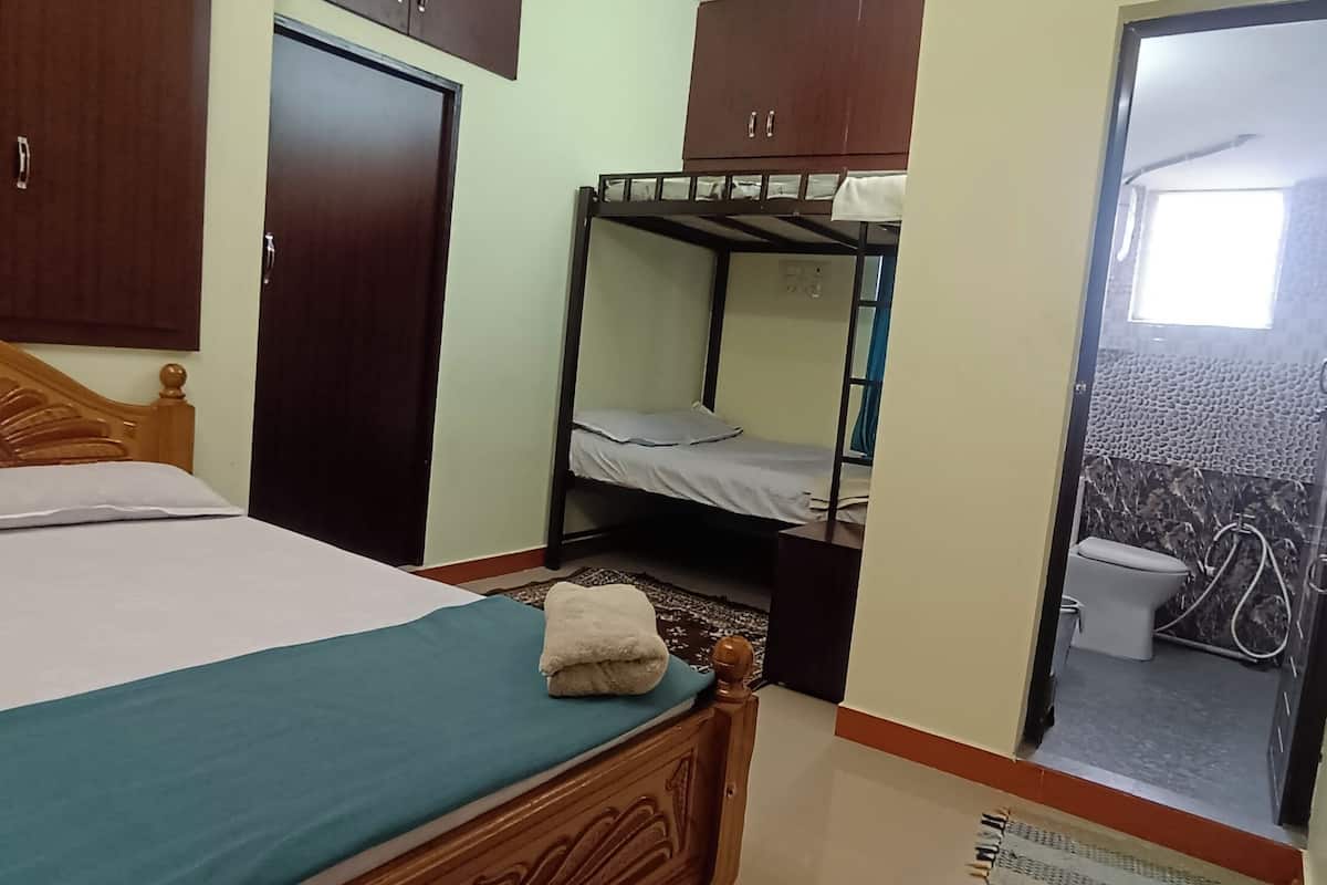 A bedroom with a single bed, a bunk bed, wooden wardrobe, and a bathroom visible through an open door.