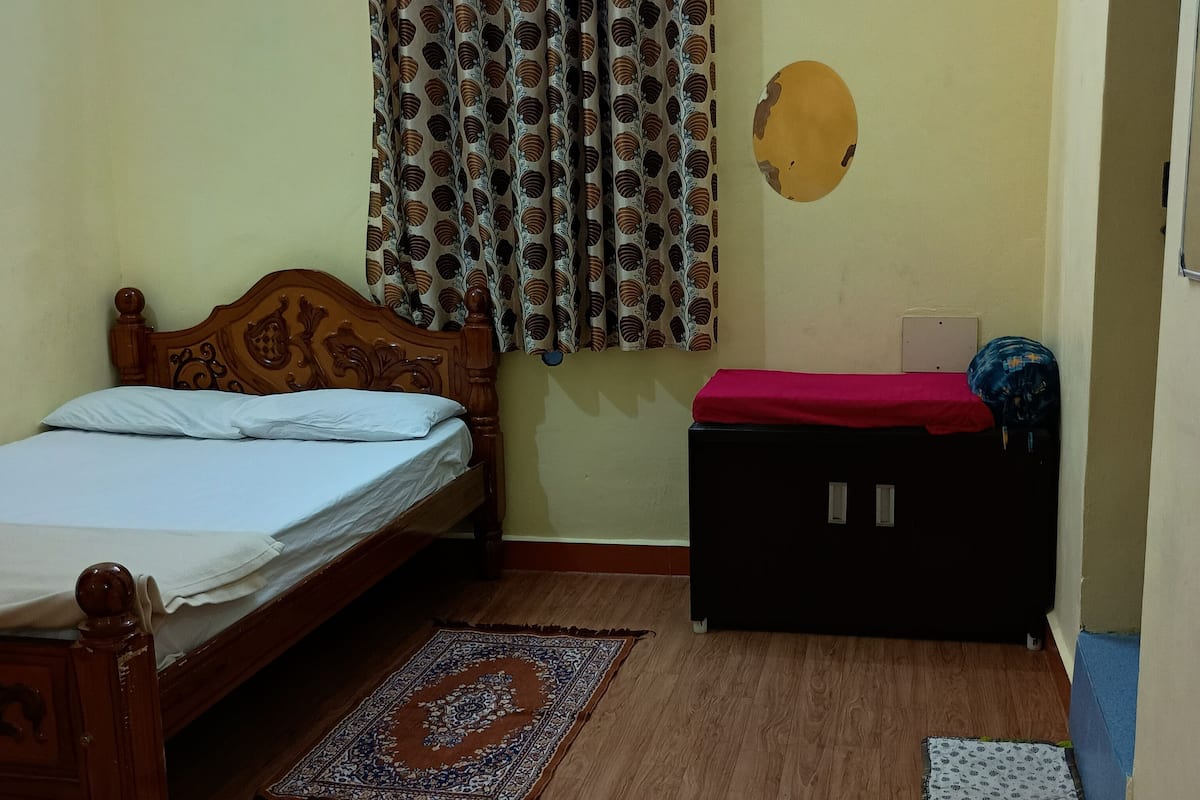 A bedroom with a wooden bed, a red bench, a patterned rug, and a wall with a circular decoration.