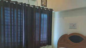 Een slaapkamer met een houten bed, een raam met donkere gordijnen, een airconditioning en een wandcontactdoos.