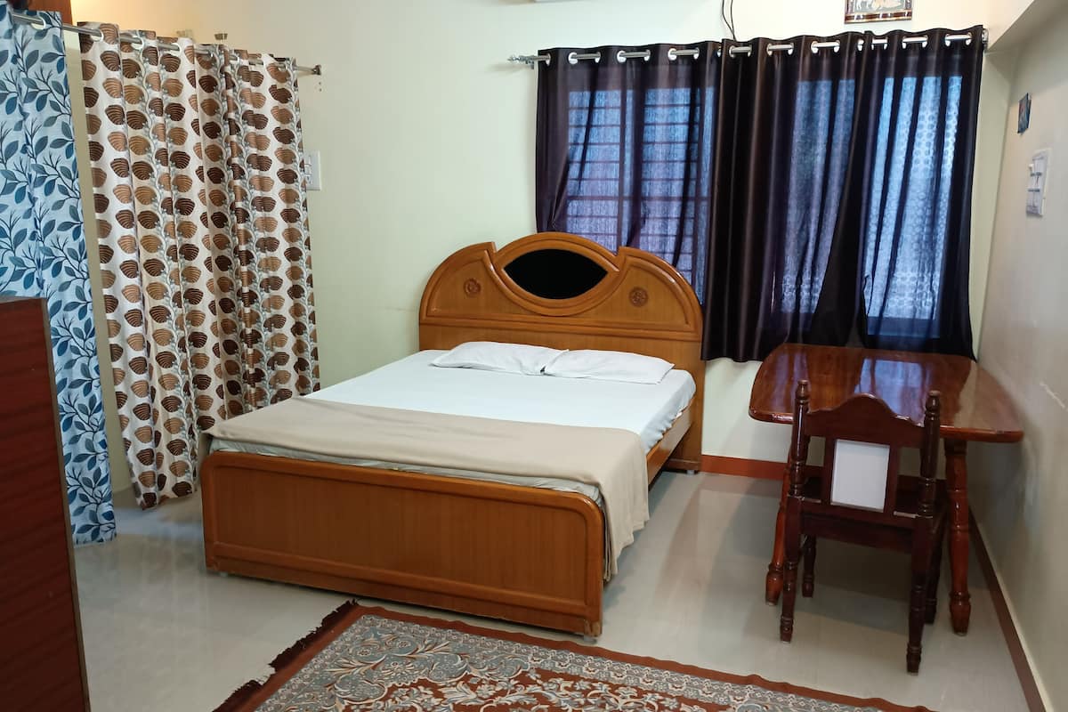 A room with a wooden bed, a desk, a chair, patterned curtains, and a patterned rug.