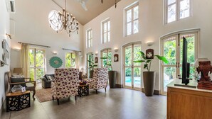 Uma sala de estar ampla, com pé direito alto, janelas grandes e um lustre.
