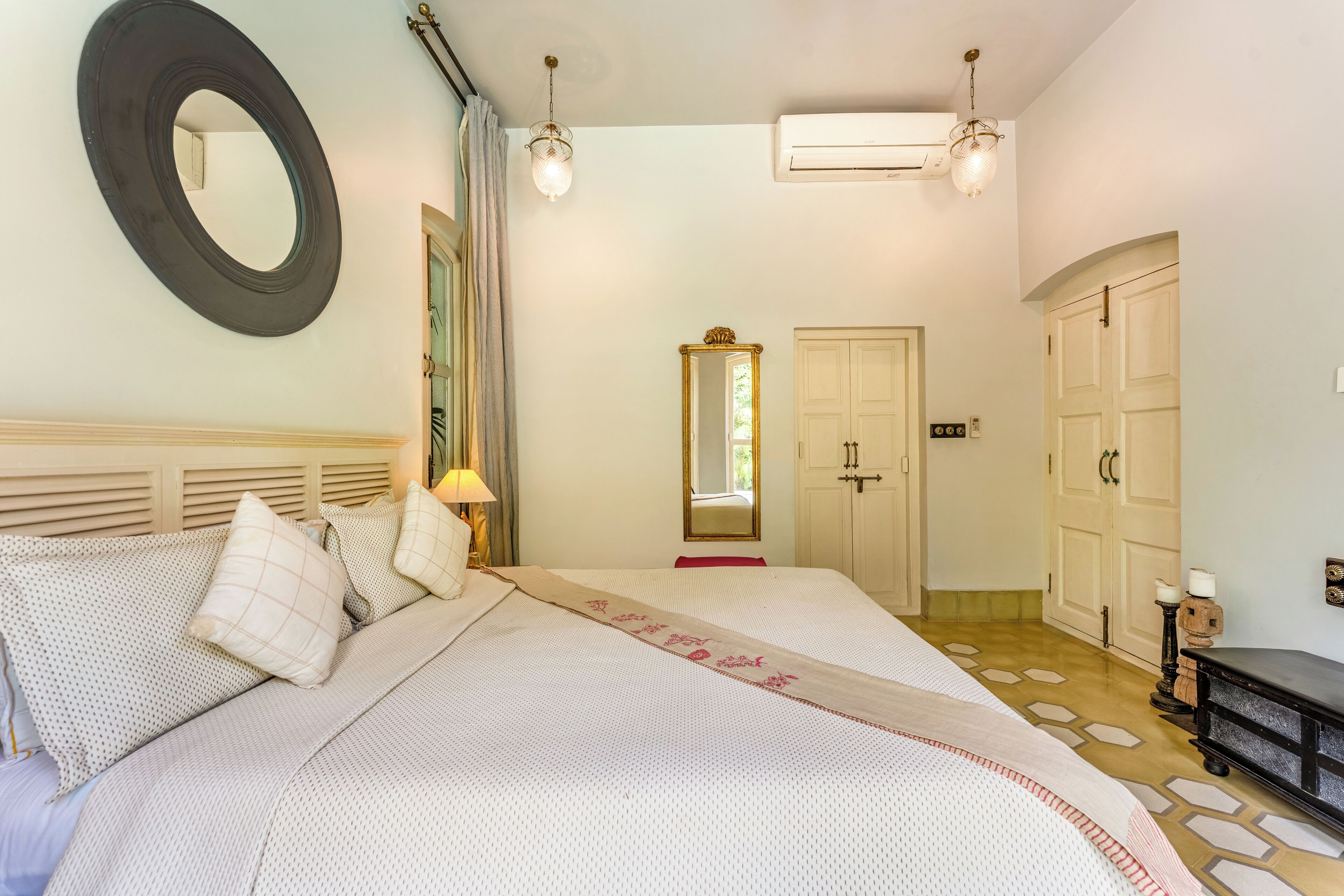 A bedroom with a large bed, a round mirror, a wardrobe, and an air conditioning unit.