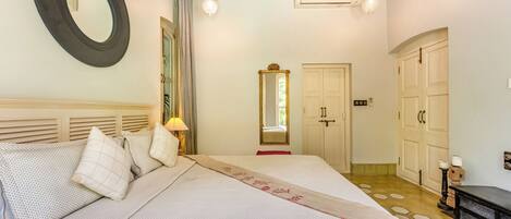 Une chambre avec un grand lit, un miroir rond, une armoire et un appareil de climatisation.
