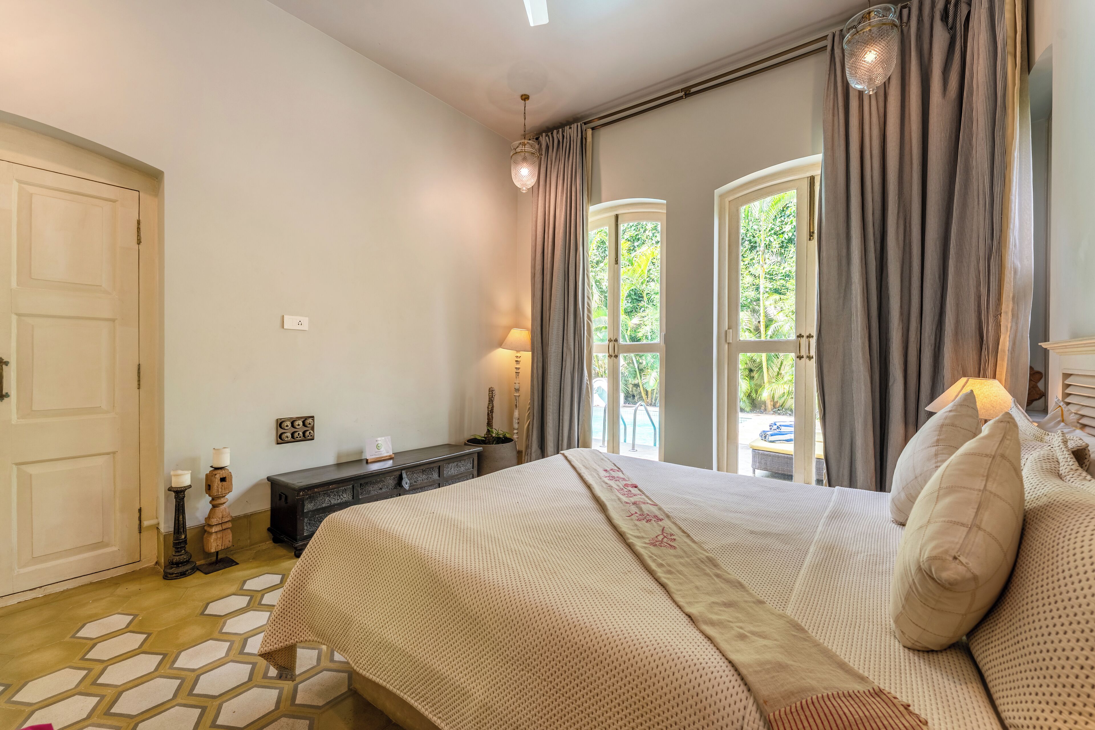 Une chambre à coucher avec un grand lit, une commode, une lampe et une vue sur l’extérieur par une fenêtre.