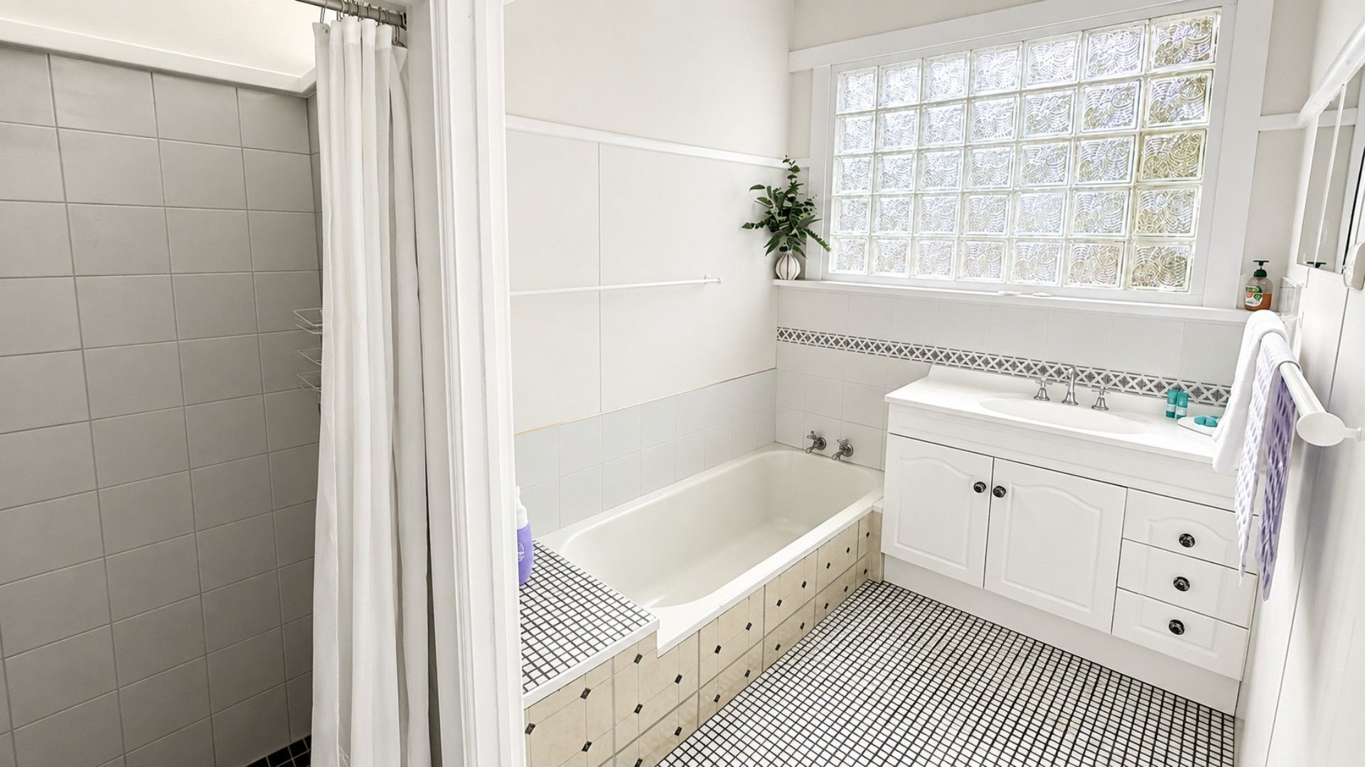 Un baño con bañera, lavamanos y ventana con vidrio decorativo.