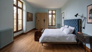 A bedroom with a large bed, wooden floor, a radiator, a wardrobe, and a window.