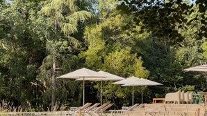 A pool area with umbrellas, lounge chairs, and a stone wall. - Wild Elegance: A 120-Acre Forest & Château (Mouleydier)