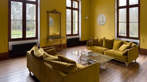 A room with yellow walls, large windows, a sofa, a table, and a mirror.