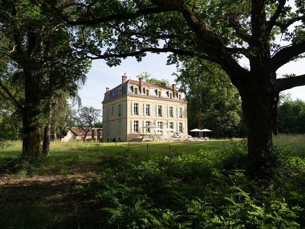 Ein großes, mehrgeschossiges Gebäude mit einer symmetrischen Fassade, umgeben von üppigem Grün und Bäumen.