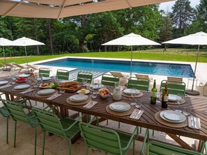 Ein Essbereich im Freien mit Pool, grünen Stühlen und weißen Sonnenschirmen.