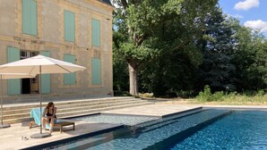 A swimming pool with clear water, a bench, and an umbrella. - Wild Elegance: A 120-Acre Forest & Château (Mouleydier)