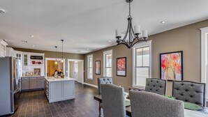 A spacious kitchen with a central island, dark flooring, and a dining area with upholstered chairs and a chandelier. - Peaceful, Serene Getaway 17 Mi to Dtwn Roswell! (Roswell)