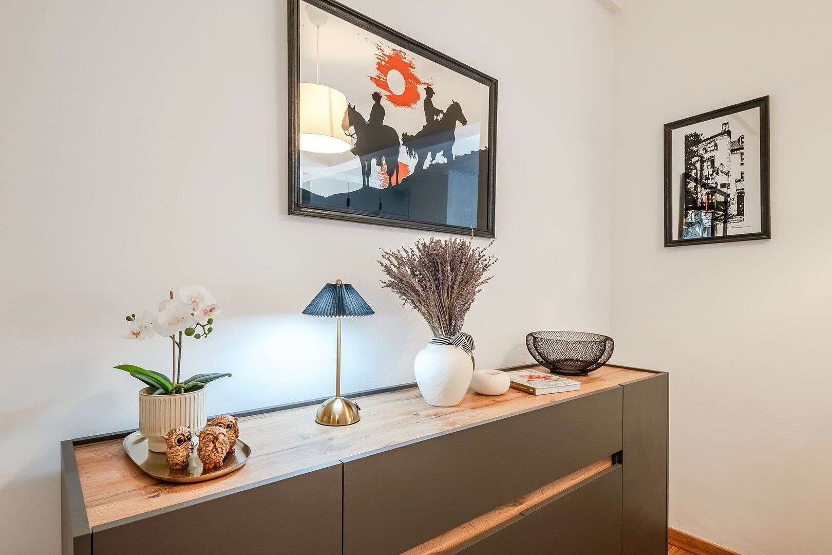 Una sala de estar moderna con una consola de madera, un cuadro enmarco, una lámpara y objetos decorativos.