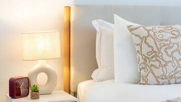 A neatly arranged hotel room with a bed, a bedside lamp, a clock, and a small potted plant.