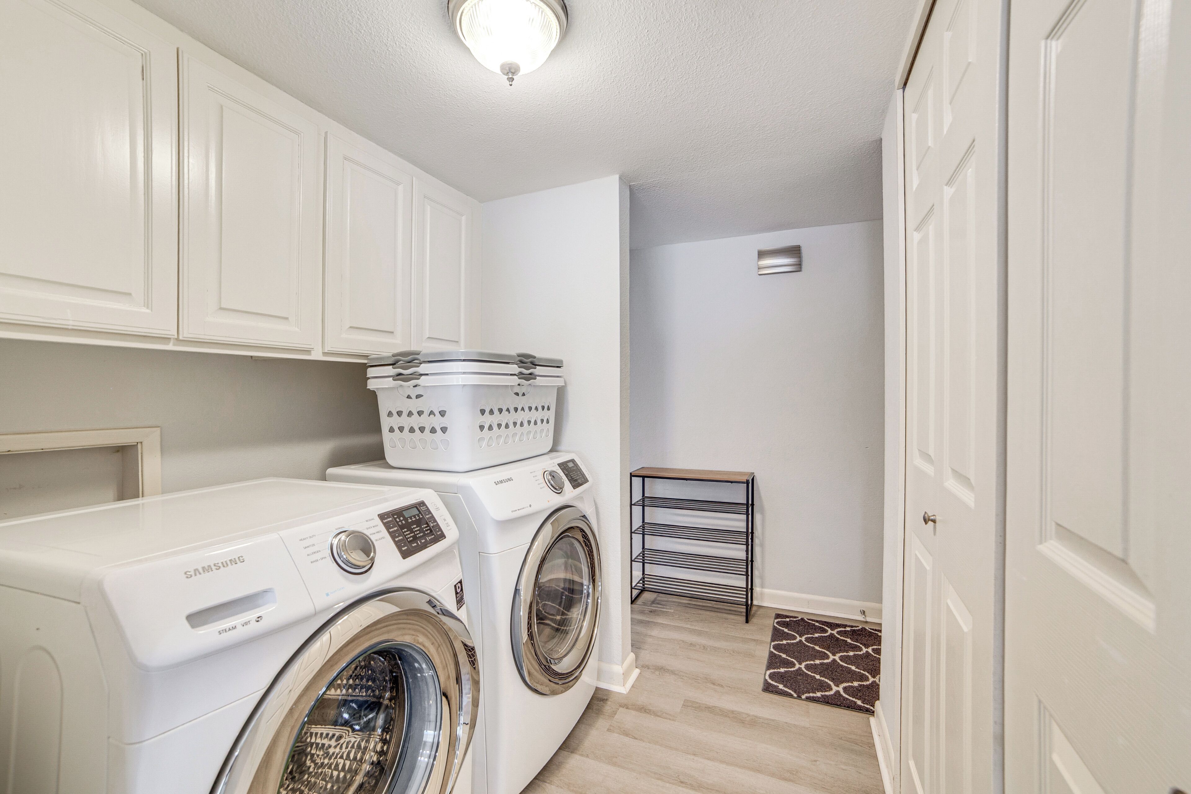 A laundry room with a Samsung washer and dryer, a drying rack, and a small shelf with baskets.