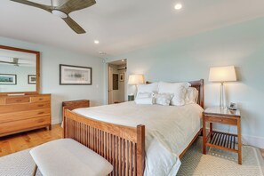 Een slaapkamer met een houten bed, nachtkastje, bankje, dressoir en plafondventilator.