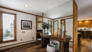 Un espacio habitable amplio con piso de madera, un ventanal grande, una mesa de comedor y una cocina visible a través de una puerta abierta.